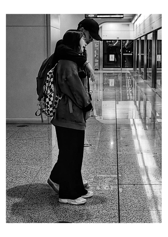 一张黑白照片 一位女士背着书包 正在走下走廊 看着手机。