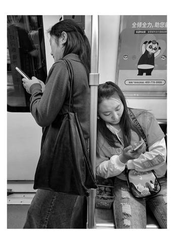 一个年轻女子坐在地铁或火车上 正在看手机 另一个年轻女孩站在她旁边。