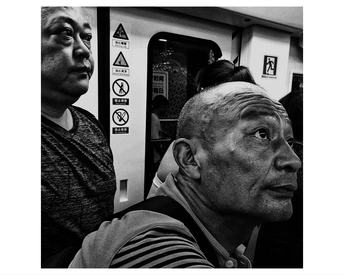 一张黑白照片 一位老人坐在地铁站台 一位女士站在他旁边。