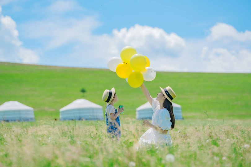 一个穿着白色连衣裙的小女孩拿着黄色气球坐在草地上