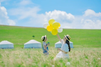 一个穿着白色连衣裙的小女孩拿着黄色气球坐在草地上
