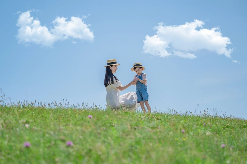 一个年轻的女人和一个小男孩手牵着手 在蓝天下开着白花的绿色田野里走下山