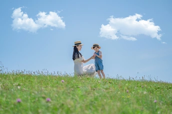 一个年轻的女人和一个小男孩手牵着手 在蓝天下开着白花的绿色田野里走下山