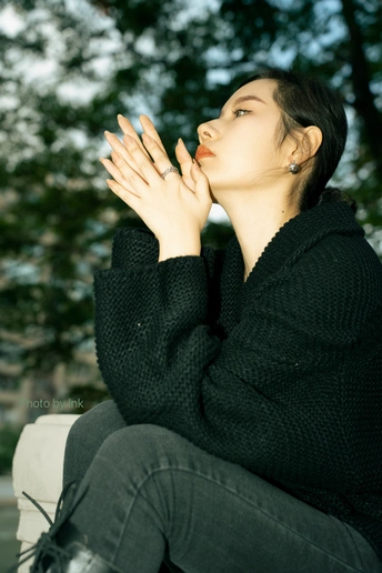 一个穿着黑色衣服的年轻女子坐在长凳上 双手合十放在前面