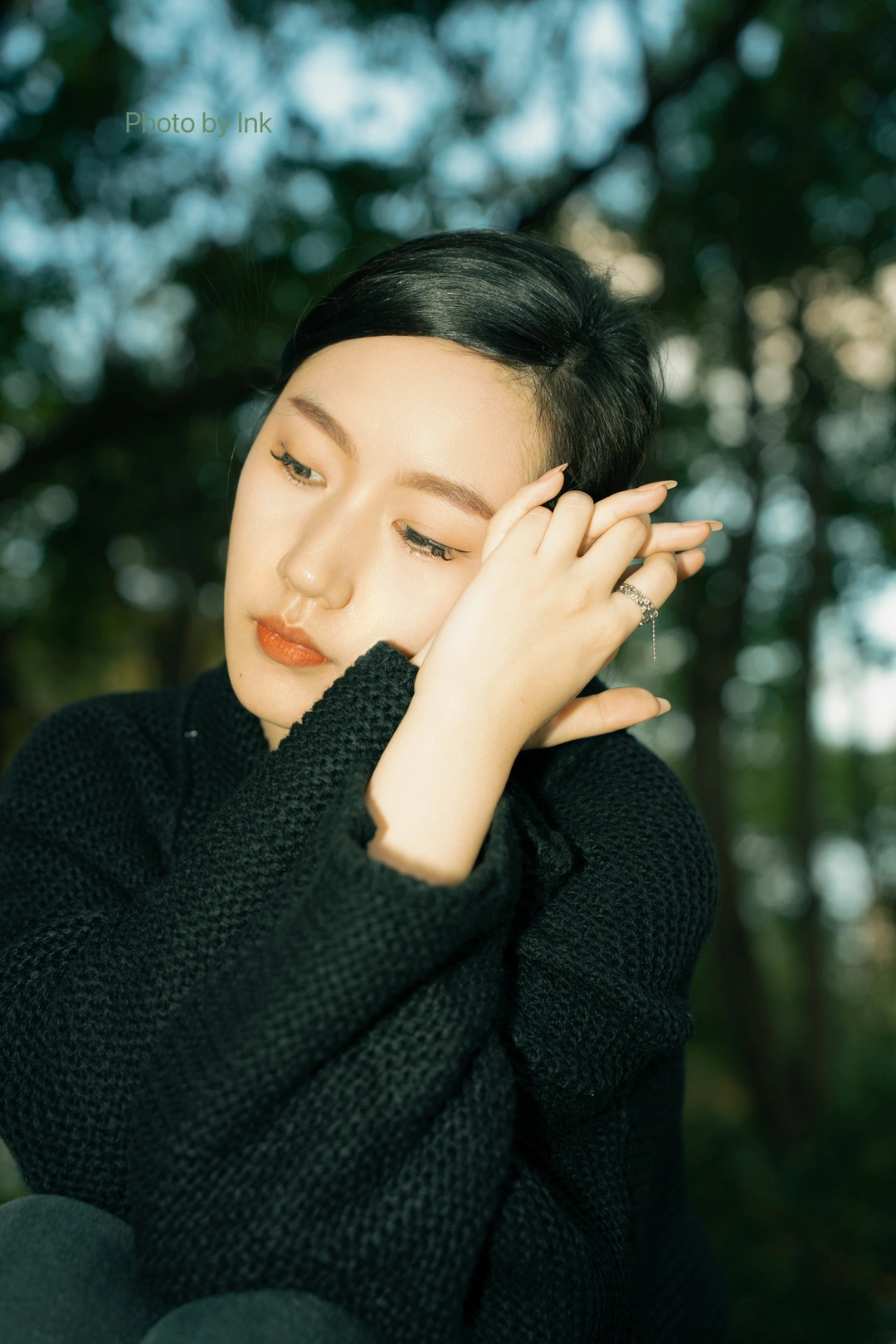 一位年轻女子穿着黑色在森林中摆姿势 双手捂住脸