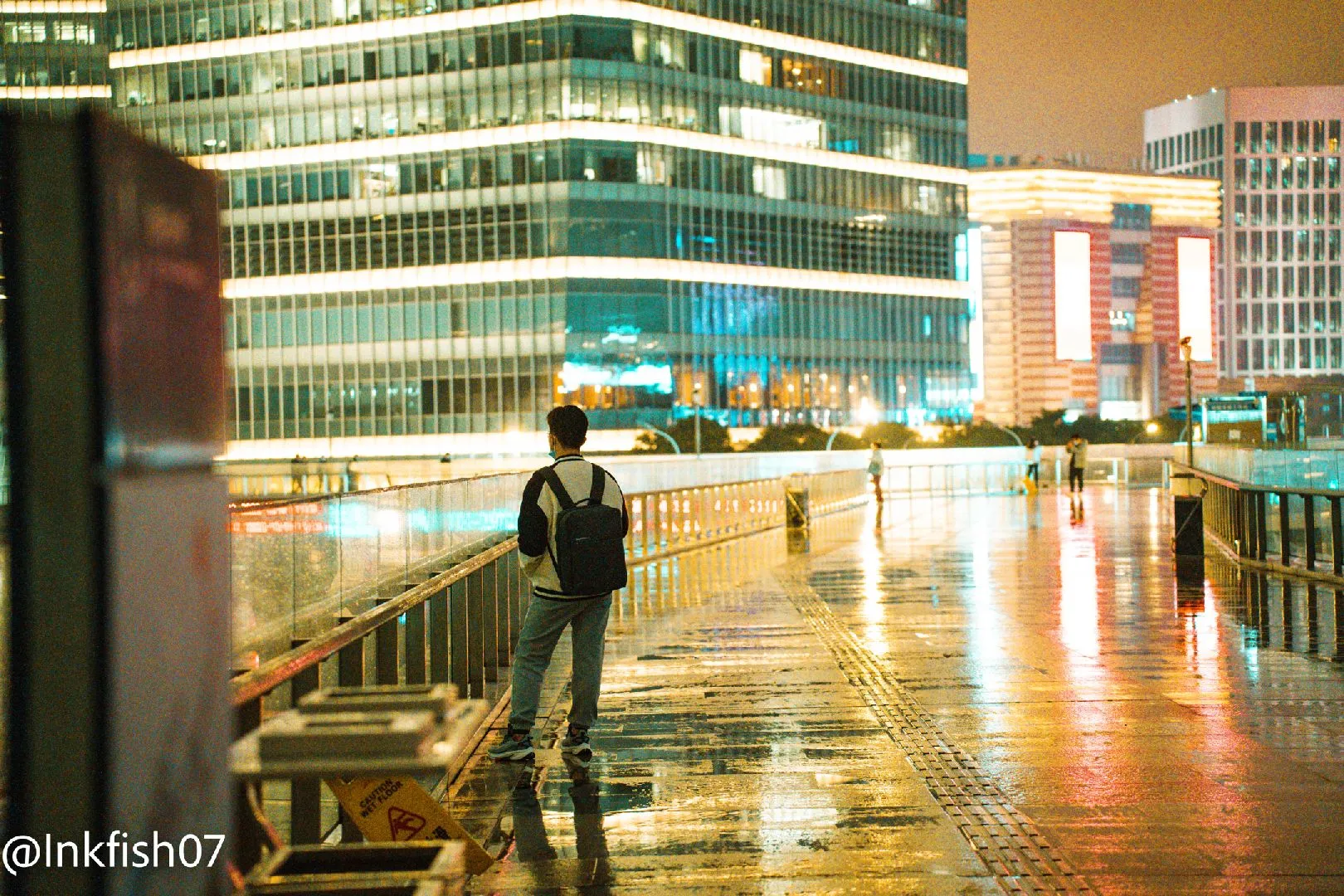 一个站在雨夜湿漉漉人行道上的男人 拿着伞。