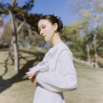 一位穿着白色连衣裙的年轻女子站在一个有树木背景的田野中