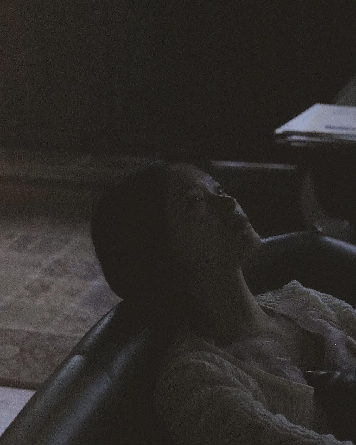 一位年轻女子躺在一间暗室的沙发上 椅子上放着一个遥控器