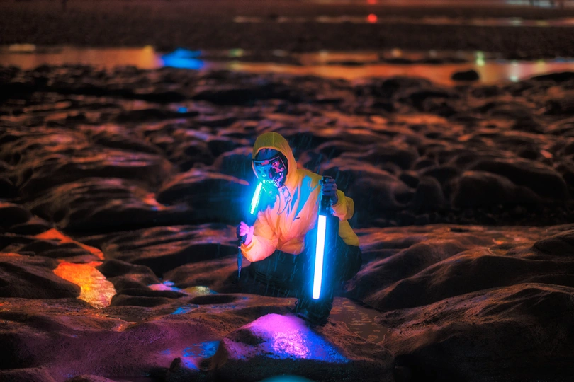 一个女人晚上在有岩石和沙子的海滩上拿着手电筒