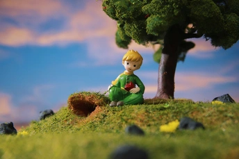 一个坐在山坡上的小男孩 周围有草地和一棵树。