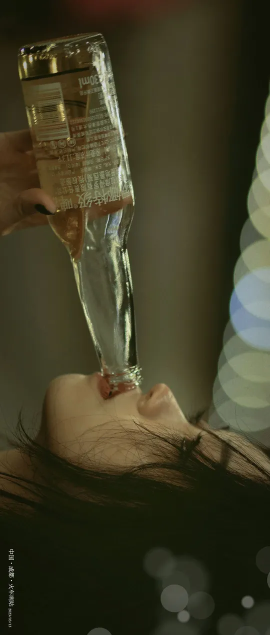 一位女子手里拿着一杯酒 前方有一瓶水。