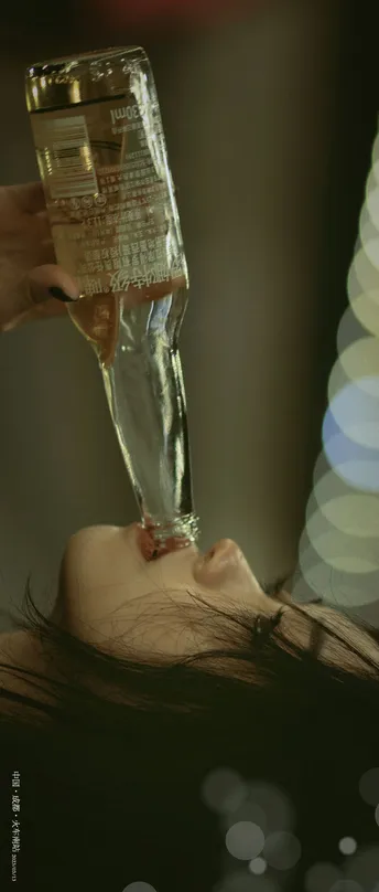 一位女子手里拿着一杯酒 前方有一瓶水。