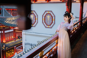 一位穿着中国传统服装的美丽年轻女士站在一栋建筑物的阳台上。
