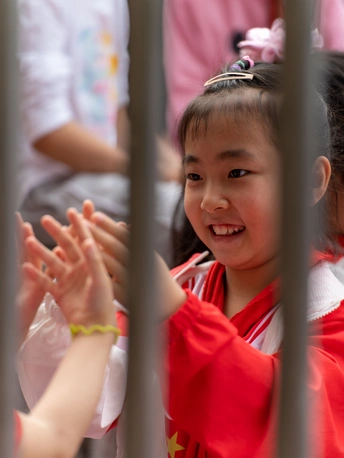 一个小女孩穿着红衬衫 通过围栏的栅栏看着另一个穿着红衬衫的小女孩。