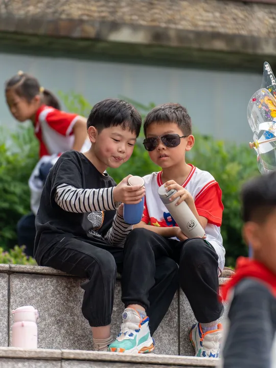两个年轻男孩坐在边缘上看着手机 背景有一些人。