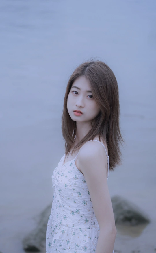 一位穿着白色连衣裙的年轻女子站在水边的一幅肖像