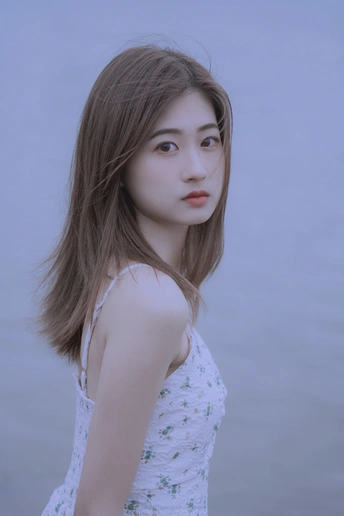 一位穿着白色连衣裙的年轻女子站在水边的人物肖像