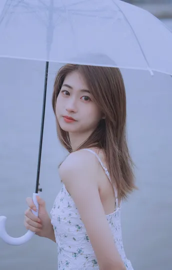 一位穿着白色连衣裙的年轻女子在雨中拿着一把透明的伞