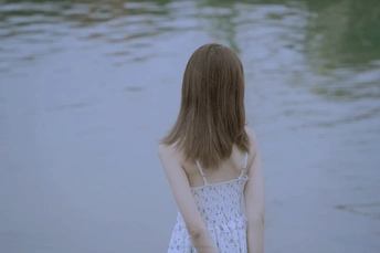 一位穿着白色连衣裙的年轻女子站在湖边沙滩上