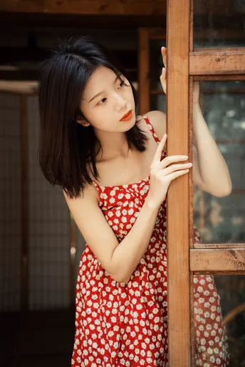 一位穿着红裙子的年轻女子正在木窗前向外看