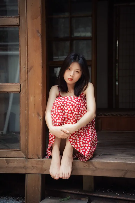 一个穿着红裙子的年轻女子坐在木质房子的门廊上
