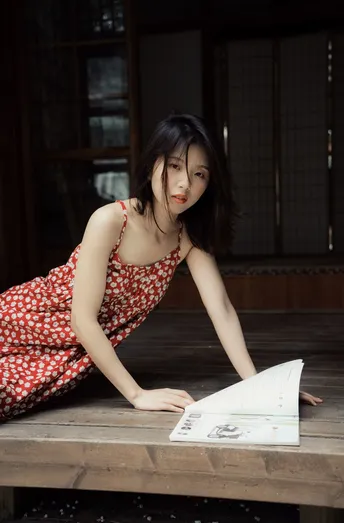 一个穿着红白裙子的年轻女子坐在木凳上 桌子上放着书和纸。