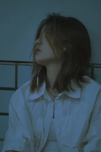 一个穿着白衬衫的年轻女子坐在蓝色的灯光下 靠近床。