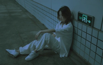 一个穿着白色裤子的年轻女子坐在一个有钟的墙壁旁边地板上
