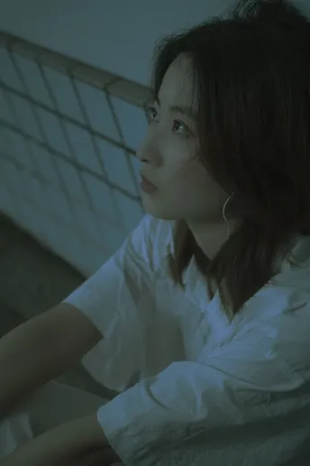 一个年轻女子穿着白色衬衫坐在床上 在一个光线昏暗的房间里 正在看笔记本电脑。
