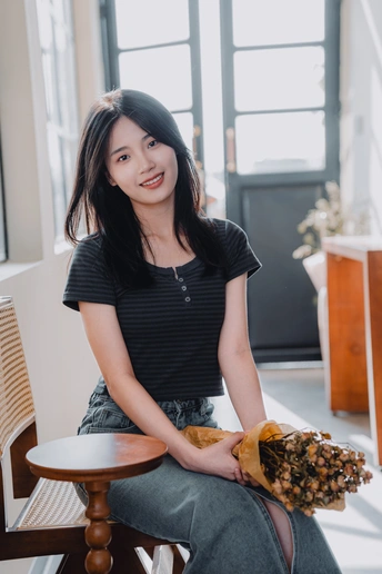 一个年轻女子坐在木制桌子旁一把椅子上 椅子上有一个松果。