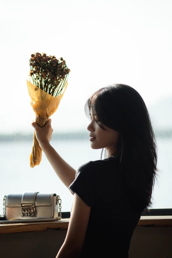 一位年轻女子抱着一束干花 凝视着窗户外。