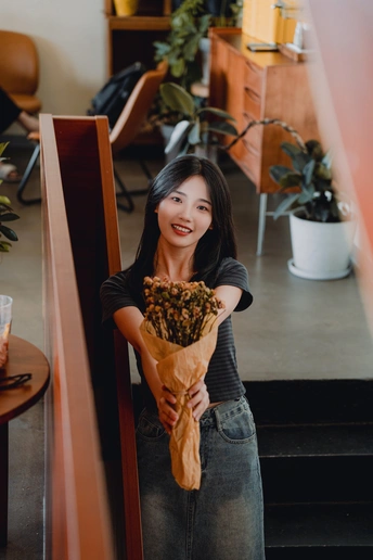 一位年轻女子手持一个装满花的棕色纸袋站在餐厅的楼梯上