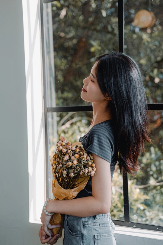 一位年轻女子抱着一束干花 凝视着窗户外。