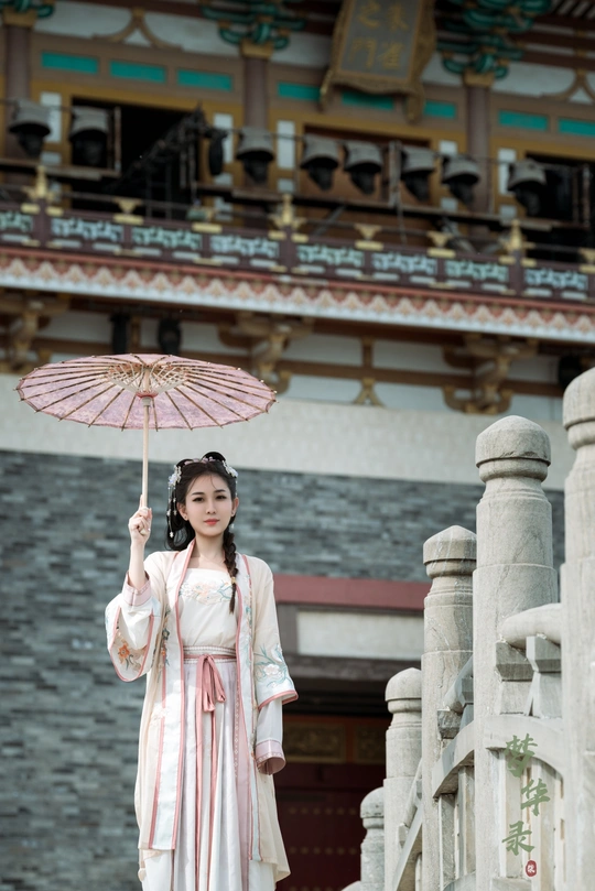 一位穿着中国传统服装的年轻女子 手持粉色雨伞 站在一栋建筑前。
