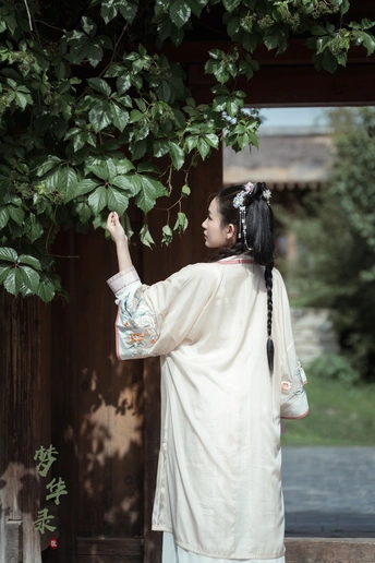 一位身着传统白色和服的年轻人站在寺庙前的一棵树下。