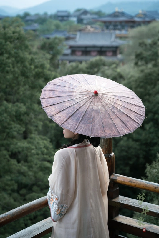 一位穿着和服的女性 手持打开的雨伞 站在阳台上。