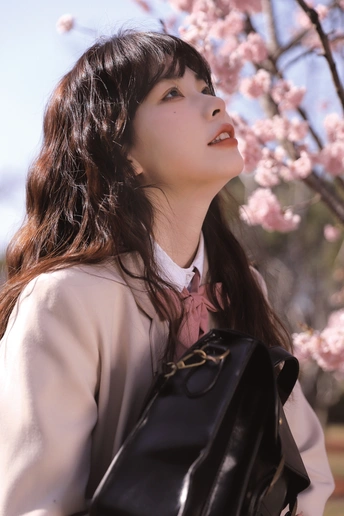 一个拿着黑色衣服的年轻女人站在一棵开着粉色花朵的树前