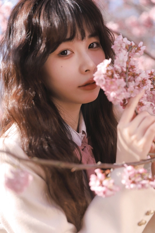 一个年轻的女人在樱桃树前把一朵粉红色的花举到脸上