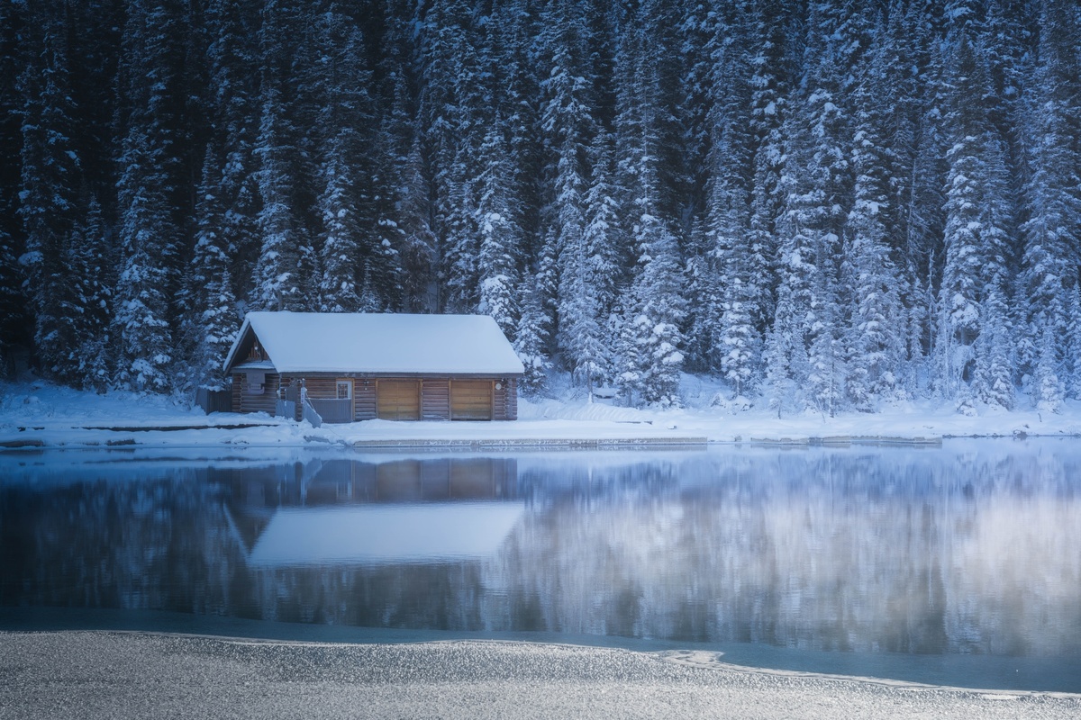在一个被雪覆盖的森林中的一个结冰的湖上的一座小木屋 地面上有雪 树上有雪。