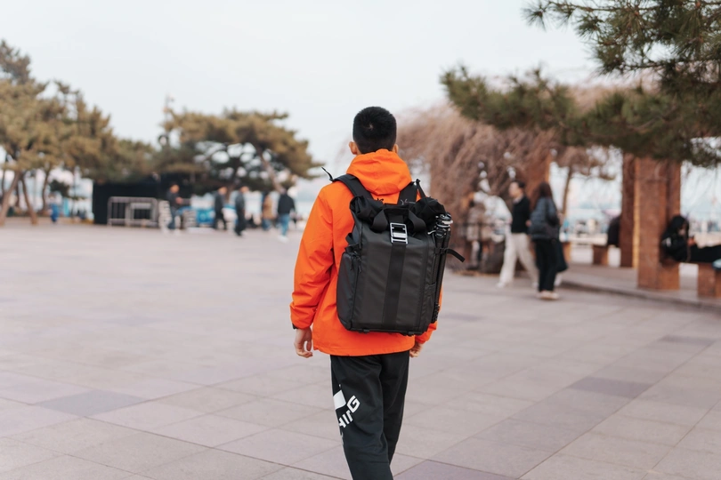 一个穿橙色夹克的男人带着背包走路