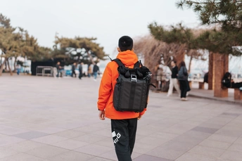 一个穿橙色夹克的男人带着背包走路