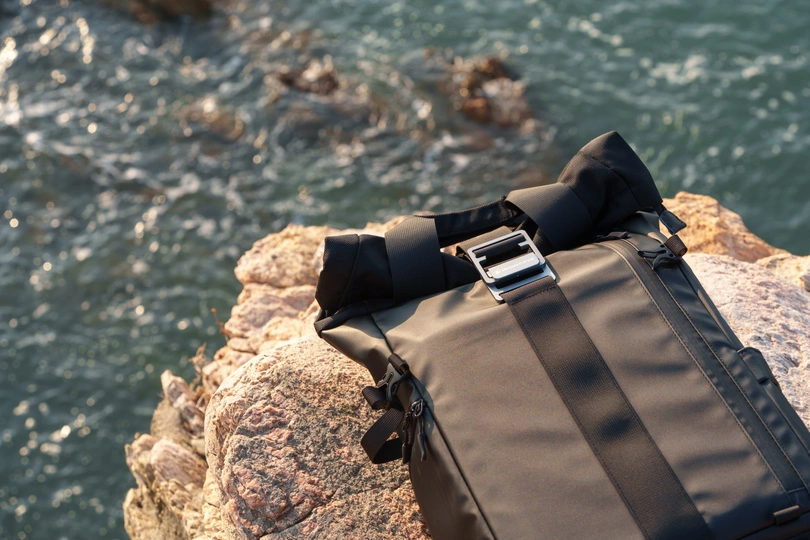 一个黑色的背包配有一条黑色 strap 悬挂在一块俯瞰海洋之水的悬崖上