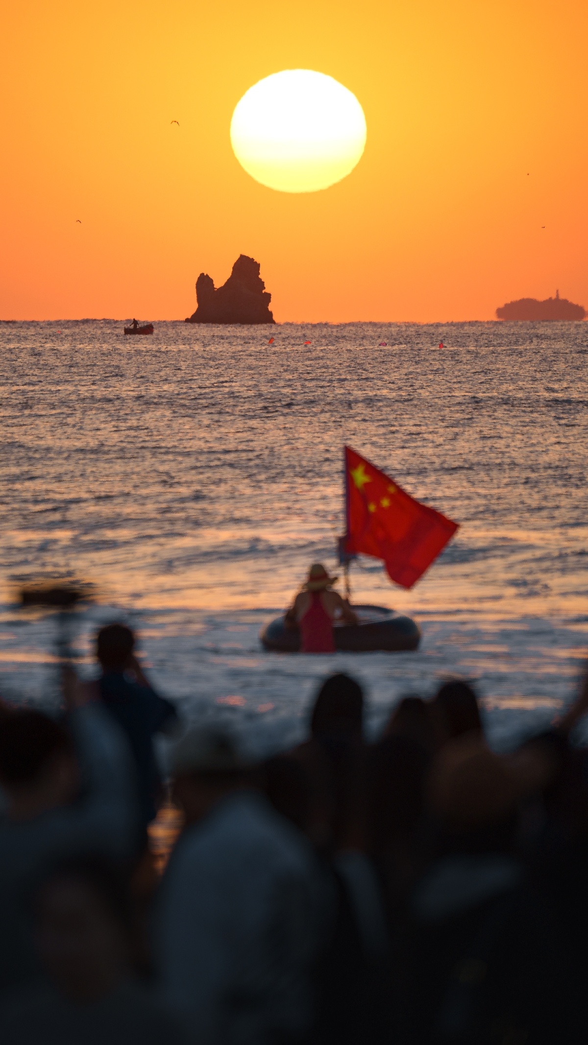 沙滩上有一群人正在观看夕阳西下时海洋上的小船。
