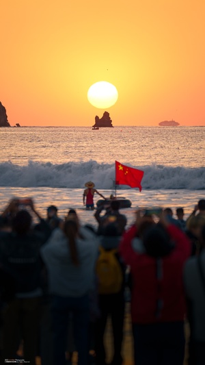 人们聚集在沙滩上观看夕阳西下时 海面上升起了红旗。