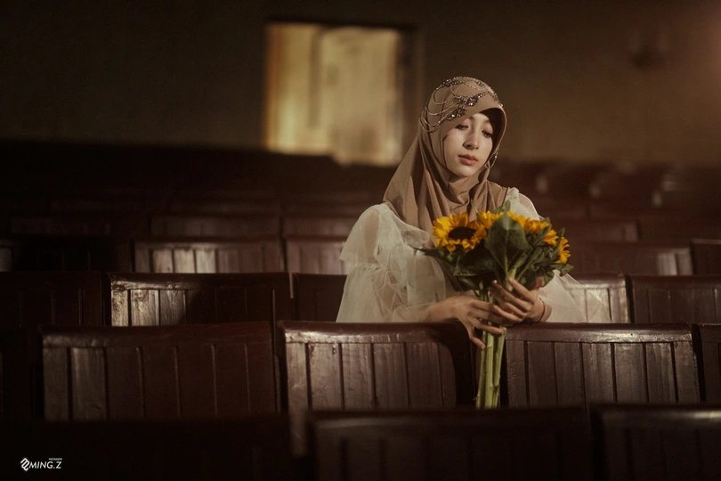 一位年轻女子抱着向日葵花束坐在教堂内 照片由<人名>拍摄。