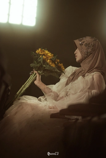 一位穿着头饰的年轻女子坐在一个黑暗的地方 手里拿着黄色花朵。