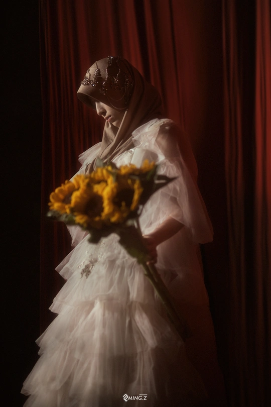 一位穿着白色连衣裙和面纱的年轻女子 手里拿着一束黄玫瑰花。