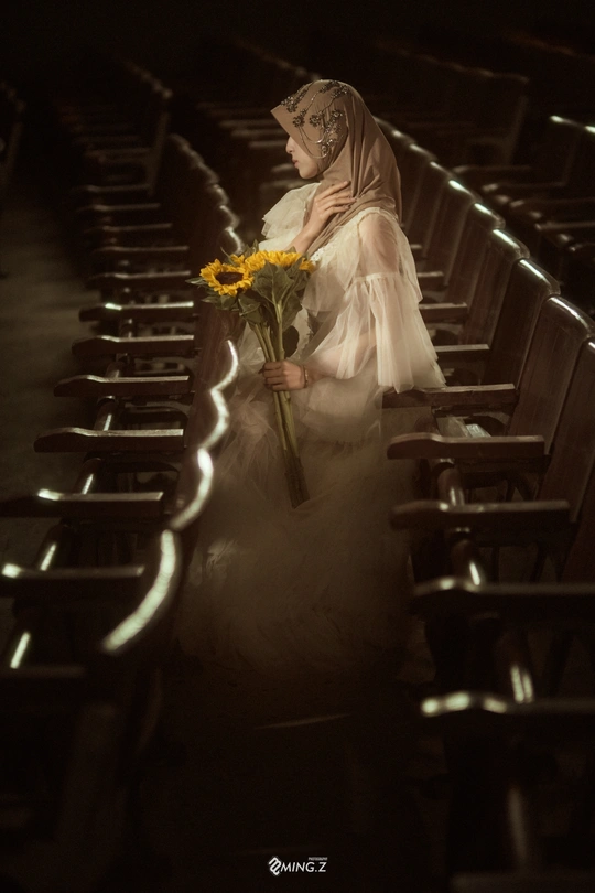 一个穿着婚纱的女孩手里拿着一朵黄色的花走在教堂的过道上。