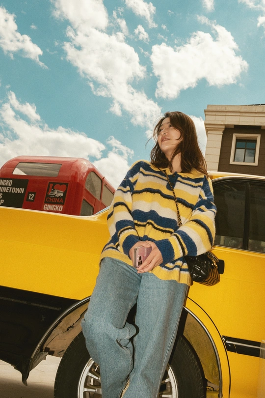 一位穿着条纹毛衣的女子靠在一辆黄色汽车上