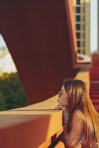一位年轻女子坐在阳台上 眺望着一座红色的桥。